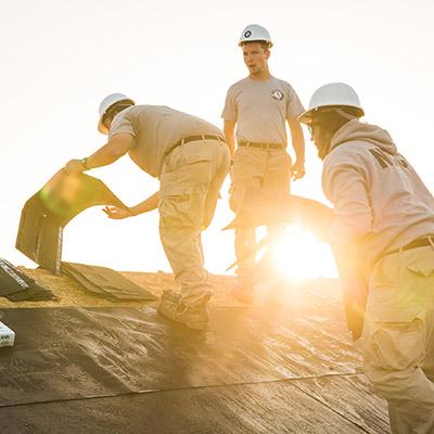 Three people laying tiles on a roof