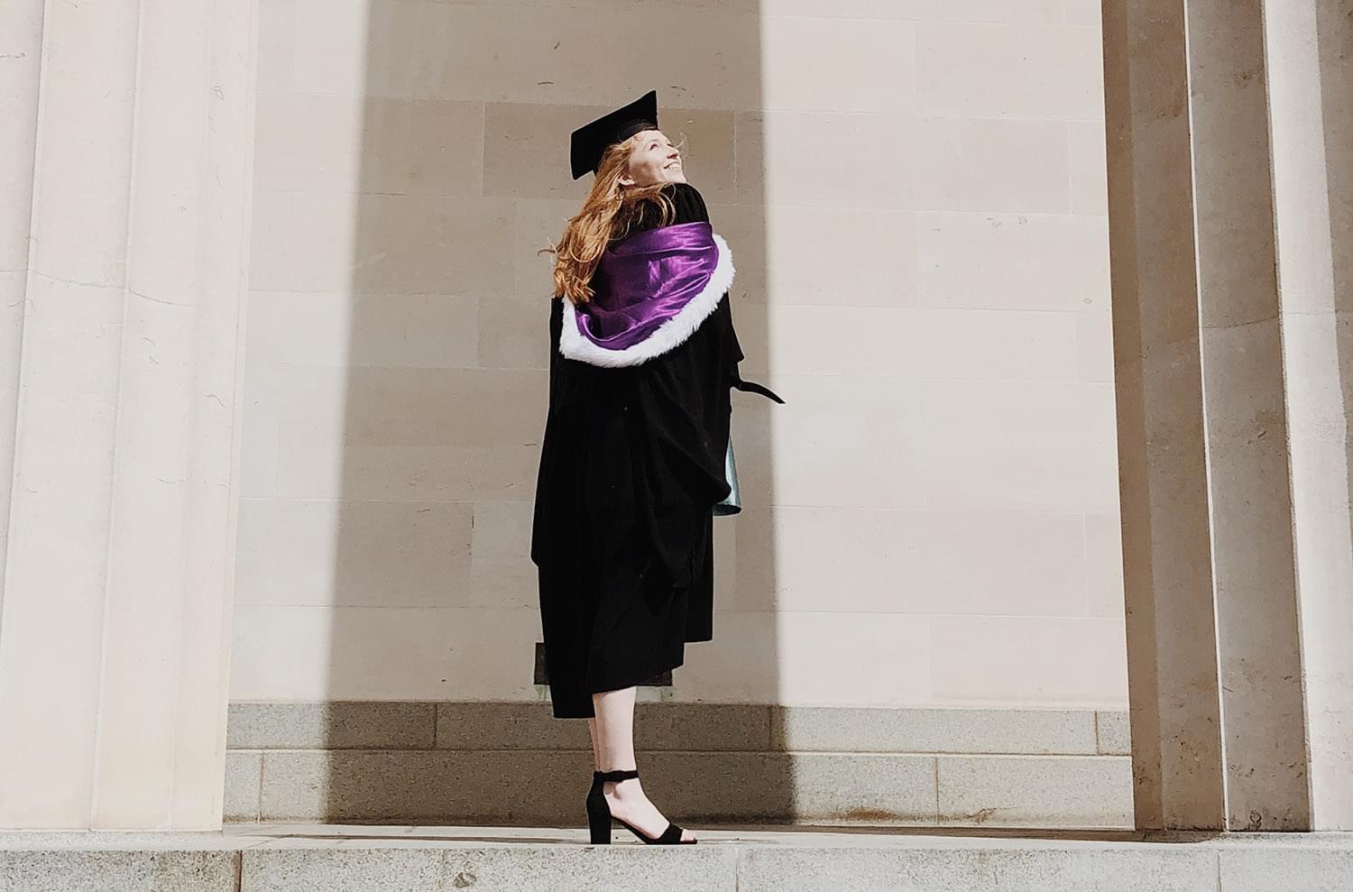 Woman wearing a mortar board hat and gown standing in front of a building