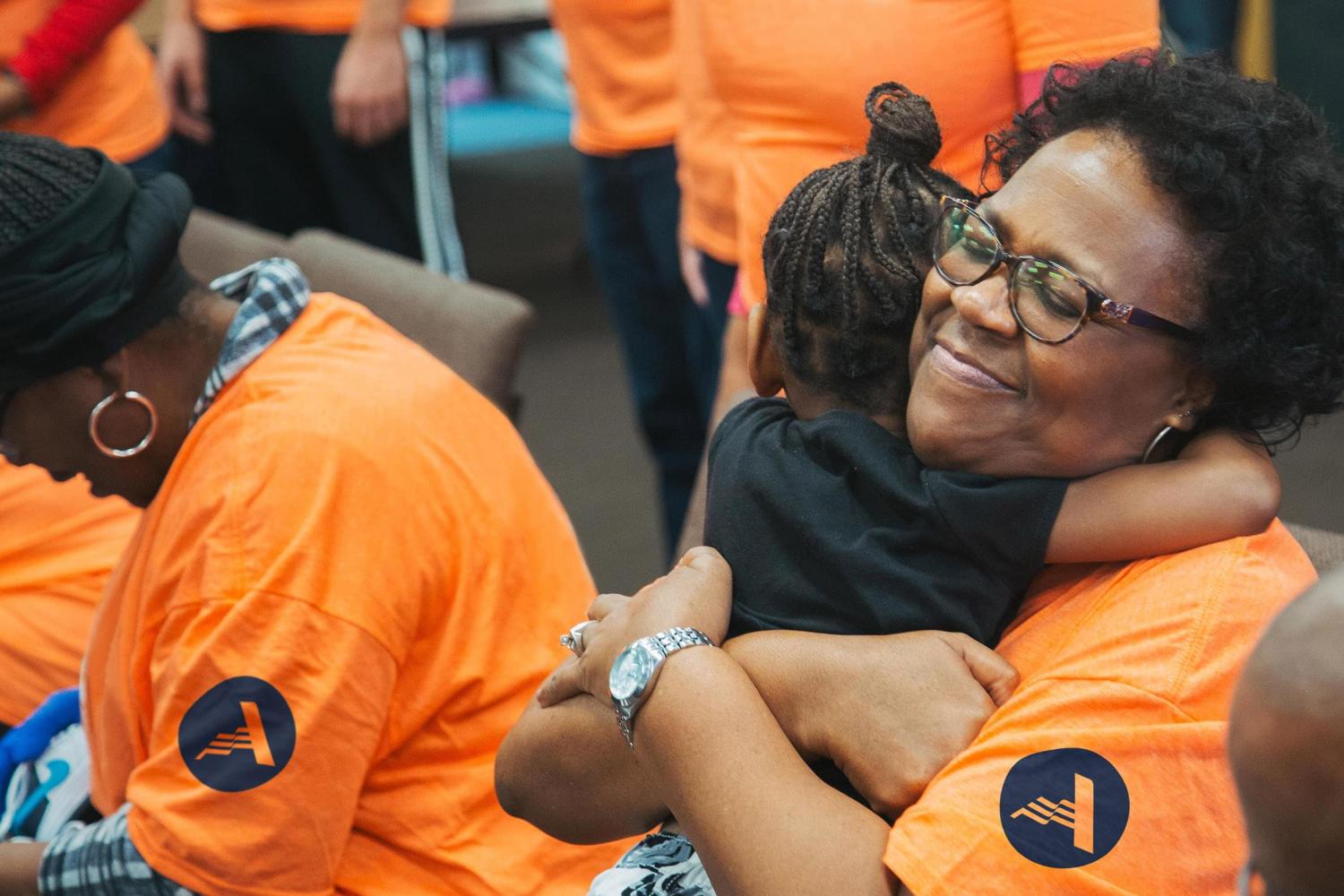 Woman wearing an orange AmeriCorps T-shirt hugging a young girl