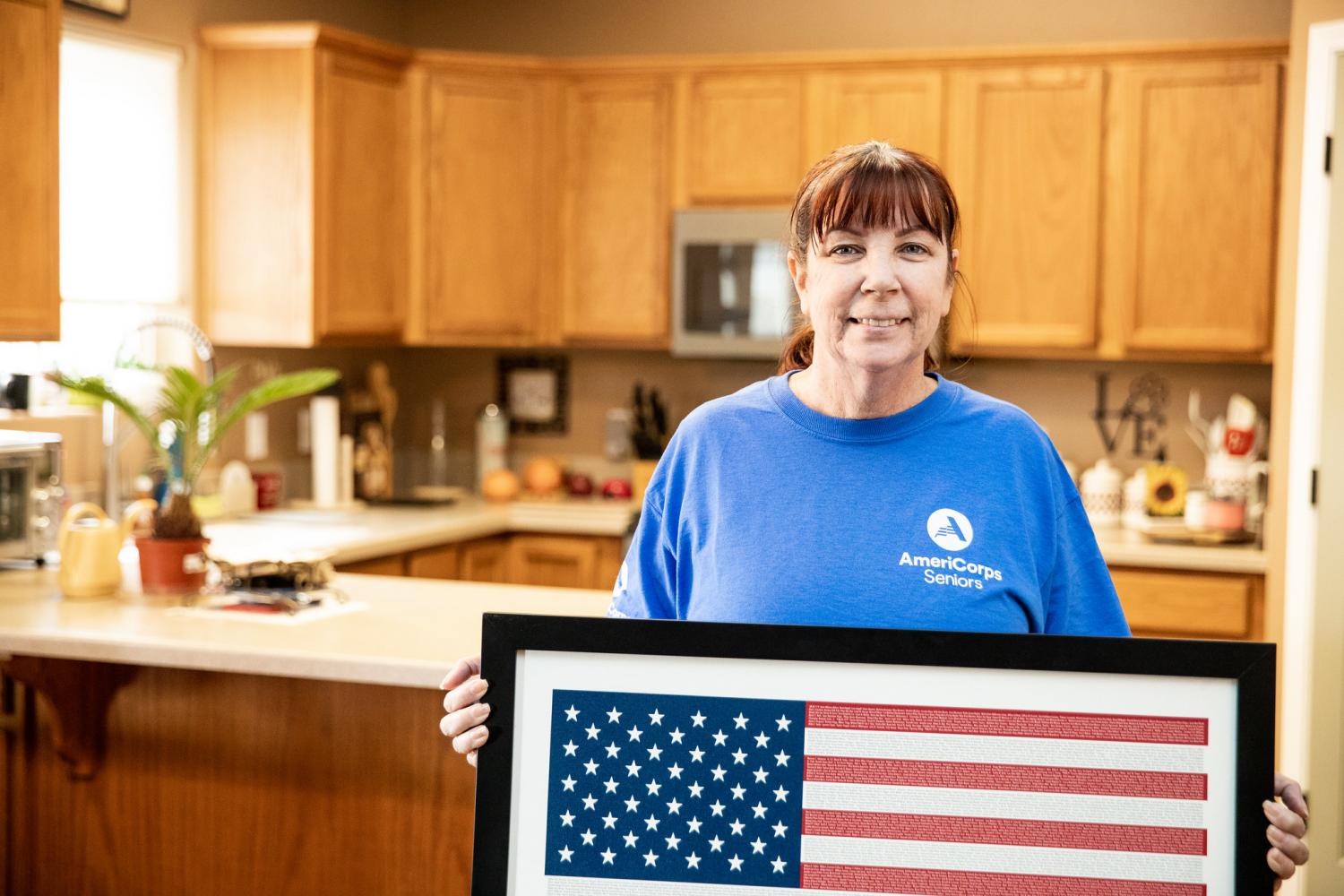 Woman in an AmeriCorps Seniors shirt stands with an American flag