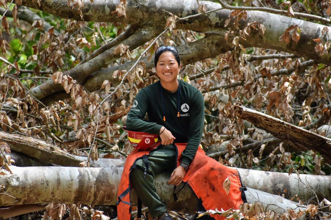 AmeriCorps NCCC member at project site sitting on fallen tree