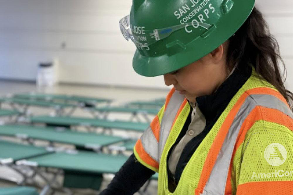 Woman wearing a green hard hat and an AmeriCorps high vis jacket