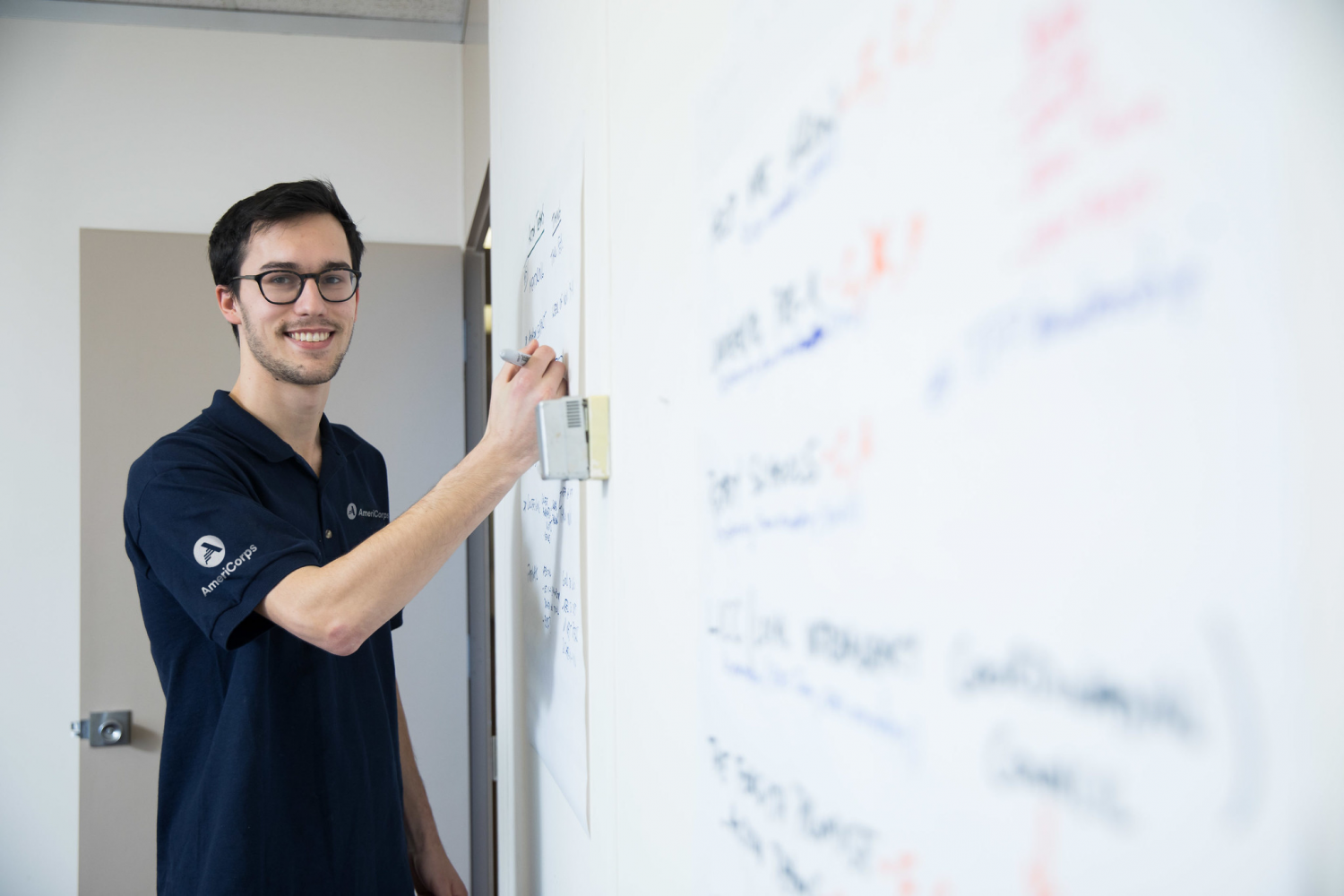 Man in an AmeriCorps stands by a whiteboard