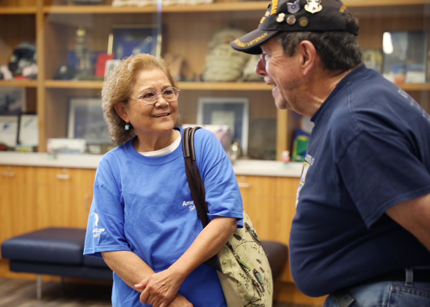 A female AmeriCorps Seniors volunteer laughing in conversation with a retired military veteran