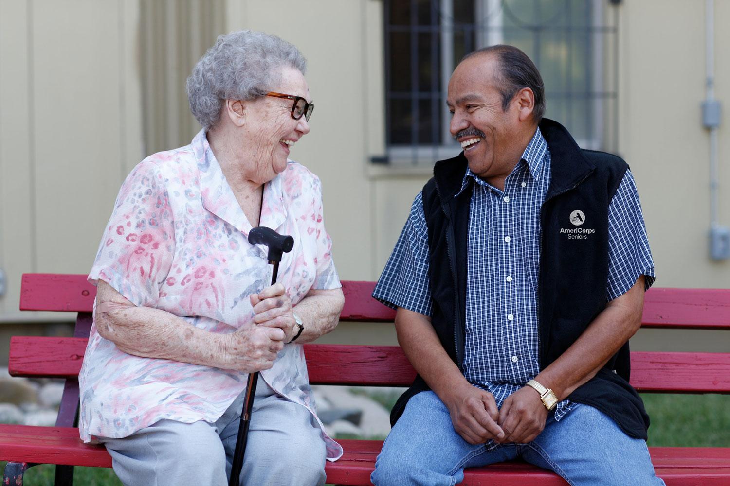 AmeriCorps Seniors volunteer laughing with a woman on a bench