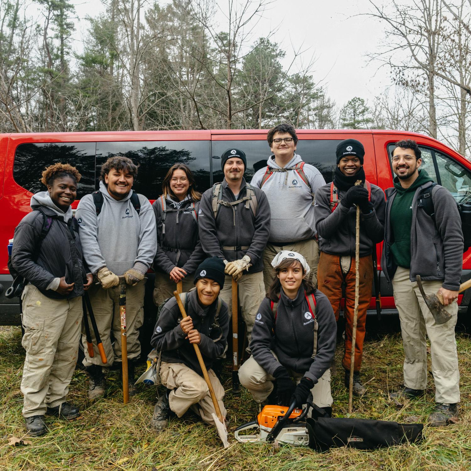 AmeriCorps NCCC team stands in front of red, 15-passenger van