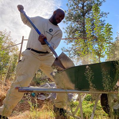 Traditional Corps member shoveling dirt out of wheelbarrow